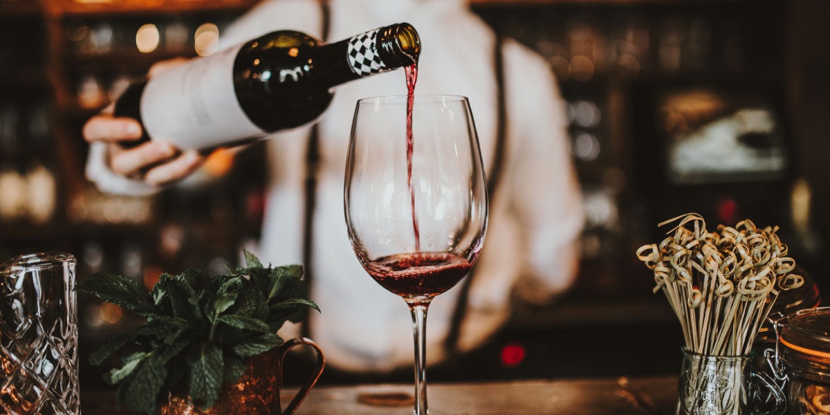 Red wine being poured into a glass at a bar