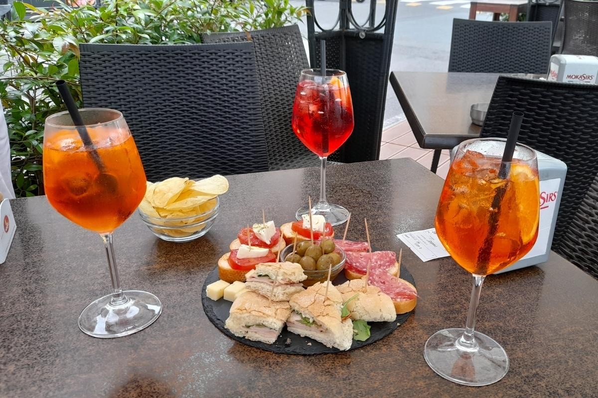Two spritzes and a plate of aperitivo snacks on a terrace table